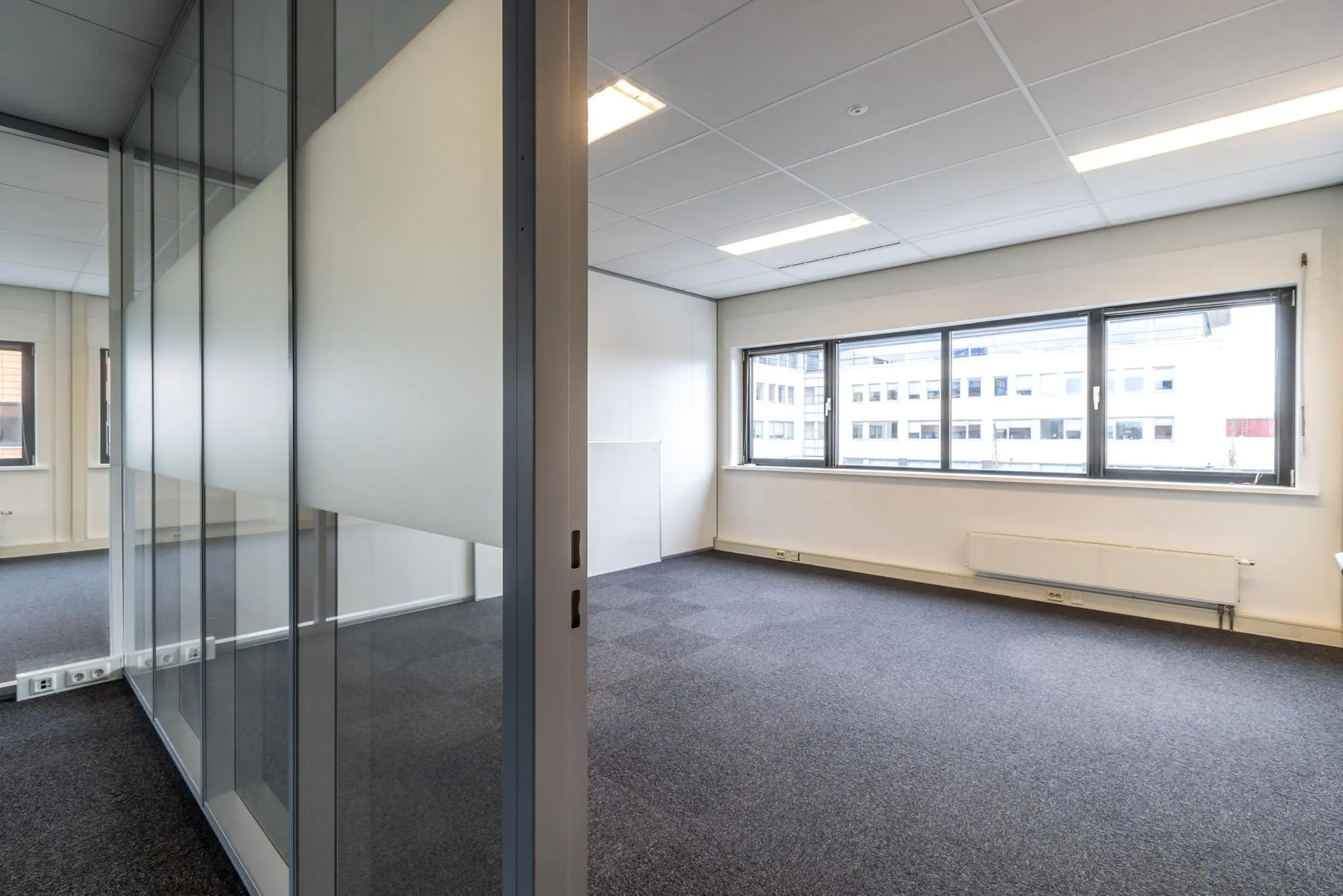 Leeg kantoor met tapijtvloer, systeemplafond en grote ramen aan de Lage Biezenweg.